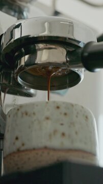 Close up of espresso extraction from bottomless portafilter into white cup.