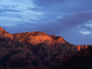 Naklejka premium Craggy mountains glow with sunset light. Clouds drift across a deepening twilight sky in Sedona, Arizona