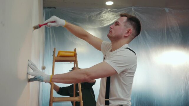 Workmen in the uniforms painting the walls with paint roller and brush in newly built house. Western style renovation. Working hard, construction roller. Slow motion, camera stabilizer shot