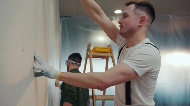 Cheerful young builders actively paint the walls of the apartment, joking and laughing. Positive emotions, good mood. Professional service. Slow motion, camera stabilizer shot