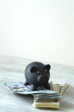 A black piggy bank sits on several stacks of dollar bills on a gray table. The setting has a simple background and good light. This shows saving money and managing finances.