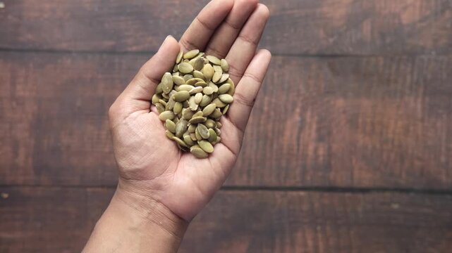 Top view of palm holding handful of roasted pumpkin seeds against wooden background