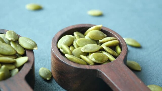 Close up of pumpkin seeds in wooden scoops on blue textured background dynamic motion