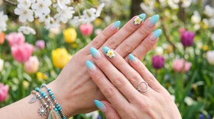 Fototapeta premium A close up view of elegantly manicured hands featuring a blue ombre design with delicate white floral 3D accents against a vibrant blurred floral garden background