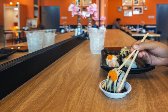 People using chopsticks to pick up sushi roll from ceramic plate with dipping sauce cup inside Japanese restaurant. Woman Customer holding sushi piece with chopsticks over soy sauce cup Japanese Food.