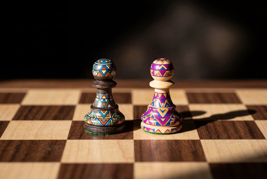 Two colorful painted chess pawns facing each other on wooden chessboard