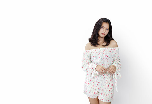 Studio portrait of a young Asian woman wearing a white off-the-shoulder floral romper, standing with a soft expression against a clean isolated white background with copy space.