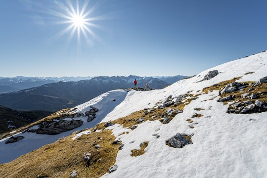 Hiker next to a cairn, in front of snowy mountains of the Rofan, hiking trail to the Guffert with first snow, in autumn, solar reflex, Brandenberg Alps, Tyrol, Austria