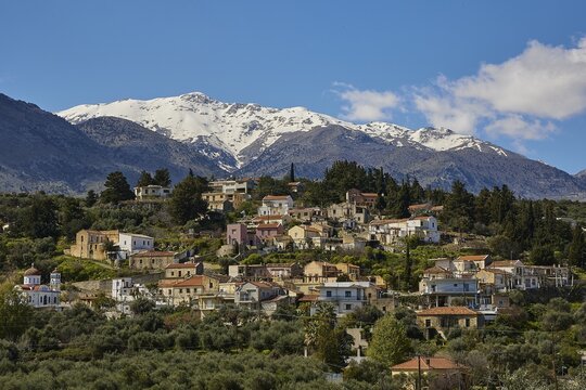 Picturesque mountain village with snow-capped mountains in the background and green vegetation under a blue sky, Lefka Ori, White Mountains, mountain massif, Paidochori village, west, Crete, Greece