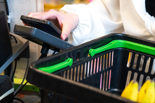 A Close-Up of a Shopper Using a Mobile Payment Device at a Checkout with a Black Shopping Basket Full of Fresh Produce.