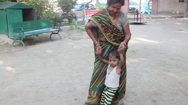 Indian grandmother helping a poor young child walk in a rural village, showing love, care, and family support in everyday life.