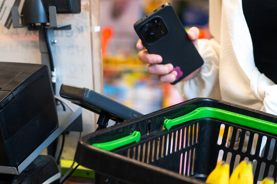 A Shopper at the Checkout: Engaging with a Smartphone While Holding a Basket in a Colorful Retail Environment.