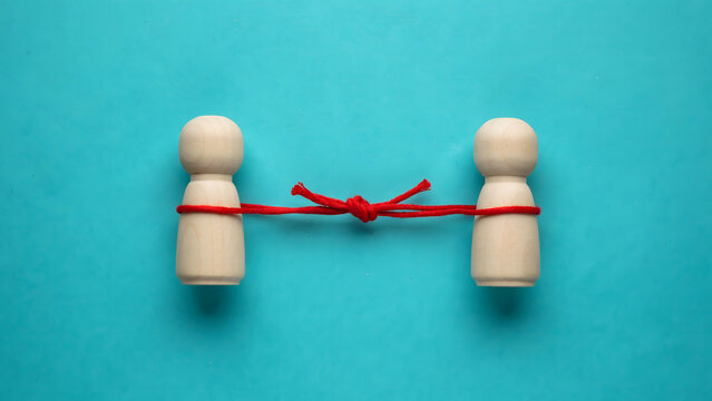 Two wooden figures connected together by a tied red string on blue background