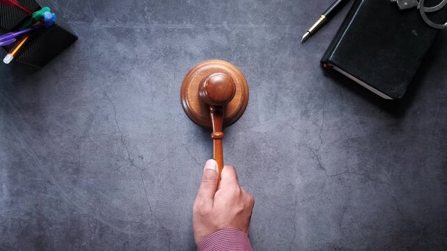 A male hand tapping a gavel, signifying a legal decision or auction close, on a dark textured background in a top-down view