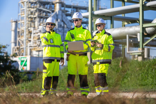 Industrial engineers with radio laptop and tablet discussing operations at an oil refinery plant, Technician and worker in high visibility workwear at large petrochemical plant site