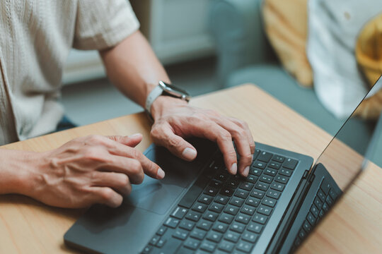 Close-up of a man hands typing on a laptop computer keyboard on desk while working from home, searching data, remote work and browsing online