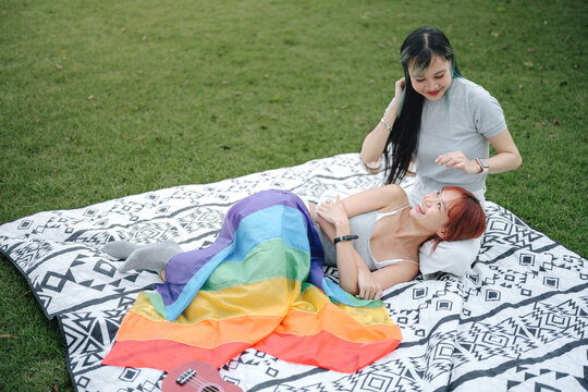 Happy Lesbian Couple Relaxing Together Under Rainbow Pride Flag During Picnic