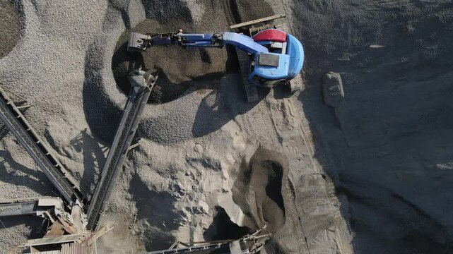 Aerial Scenery of Blue Excavator Working Near Stone Crusher and Stockpiling Area in Industrial Mine Site