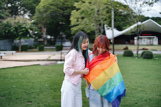Loving Same-Sex Couple Wrapping Rainbow Pride Flag Around Each Other in Public Park