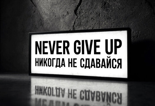 Motivational sign with never give up message in english and another language on table surface