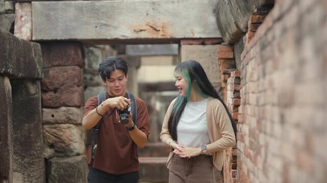 Young Asian tourist couple looking at photos on a digital camera while exploring ancient stone temple ruins on vacation.