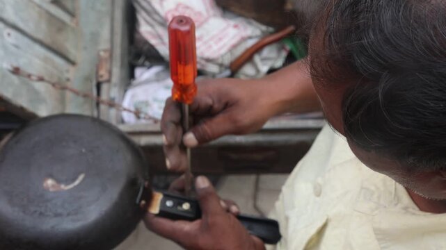 Indian Man Repairing Frying Pan Handle with Screwdriver