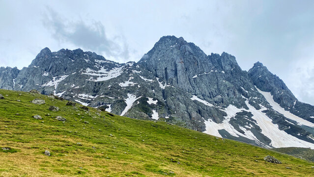 Chaukhi Mountain towers above grassy highlands and persistent snowfields in Georgia, providing a reference for climbing expeditions