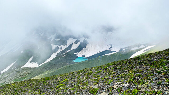 Dense fog surrounds White Abudelauri Lake and lingering snowfields in Georgia, showing rapid alpine weather, reduced visibility