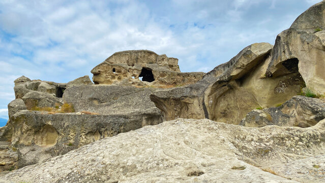 Rock-cut openings pierce the sandstone cliffs of Uplistsikhe in a low-angle view, exposing weathered chambers, ledges, and erosion patterns