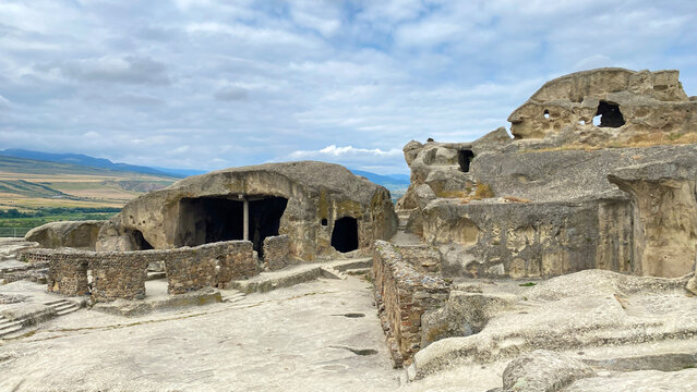 Ancient Uplistsikhe cave settlement in wide view features rock-cut halls, weathered facades, stone walls, and Georgian valley scenery