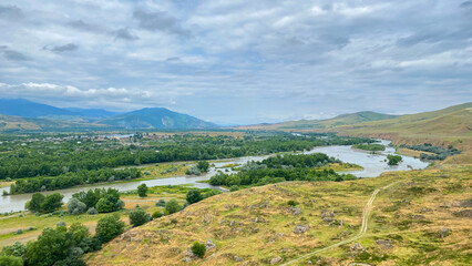 Kura River branches across a valley below Uplistsikhe in an elevated panoramic shot, linking wooded floodplains © chekart