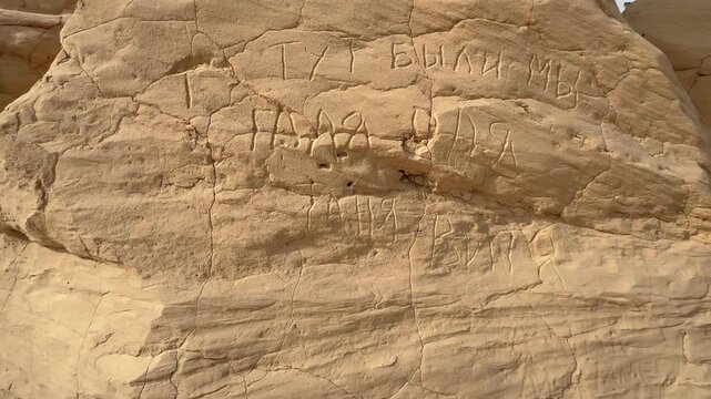 Close-up of Russian words carved into a light sandstone rock face in Debabcha, Tunisia, for use in travel or vandalism themes.