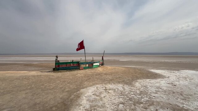Ship-shaped wooden platform with a Tunisian flag stands on the wide salt flats of Chott el Djerid under a hazy sky. Tunisia.
