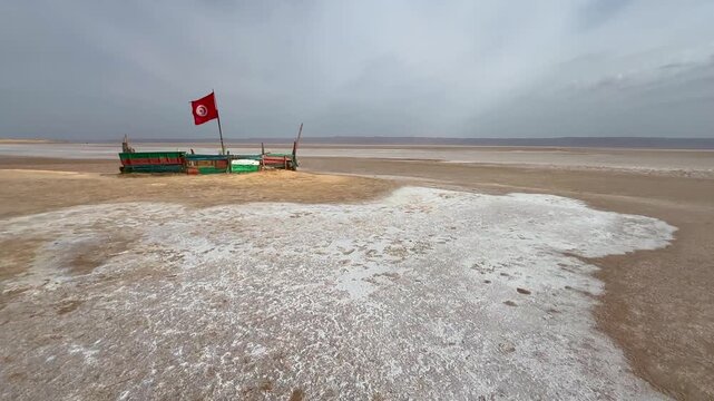 Ship-shaped wooden platform with a Tunisian flag stands on the wide salt flats of Chott el Djerid under a hazy sky, Tunisia.