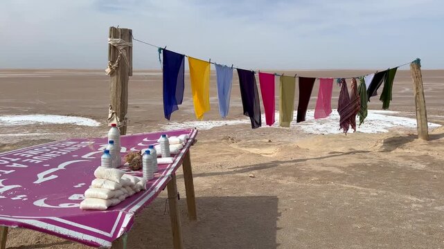 Colorful scarves hang on a line beside a simple table selling packaged salt by the dry salt lake of Chott el Djerid in Tunisia.