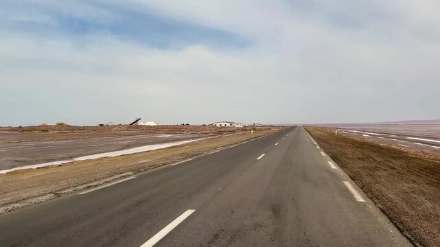Desert highway runs across the dry Chott el Djerid salt flat under a pale daytime sky. Tunisia.