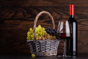 Obraz premium Red wine bottle with a glass and basket of fresh grapes
