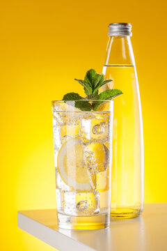Sparkling water with lemon and bottle on yellow background refreshment