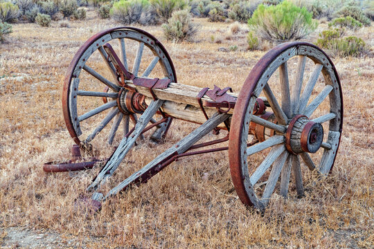Antique wagon wheels on a wooden axle in a field of dry grass