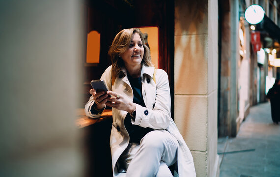 Confident woman looking away while holding smartphone at cafe bar, female traveler using mobile roaming for communication, authentic representation of business lifestyle and digital literacy.