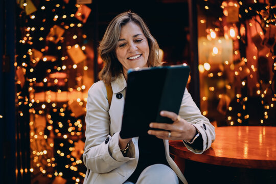 Happy Caucasian lady looking at tablet screen sitting in city cafe evening, woman using mobile application for shopping or social media, digital communication, modern gadget, lifestyle, copy space