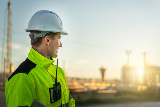Portrait of professional engineer in safety gear at oil refinery, Construction supervisor in high-visibility jacket at refinery site, Industrial worker with hard hat and radio at oil and gas plant