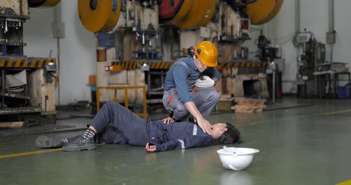  Worker helping injured colleague who collapsed on the floor after accident in factory