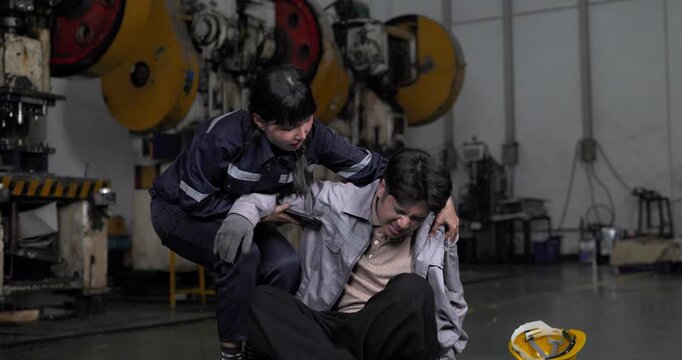  Worker helping injured colleague who collapsed on the floor after accident in factory