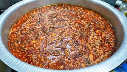 Rich Stew in Pot: Traditional Thai Red Curry Sauce with Minced Pork and Chili Oil in Big Cooking Pot. A close-up shot showcases a hearty and flavorful stew simmering in a large metal pot, its rich red © Chatchaa