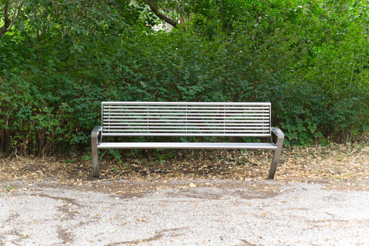 Modern metal bench in the park against green bushes