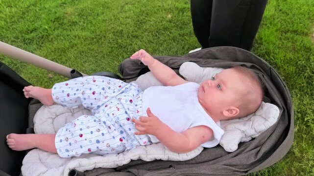 Active baby waves both arms while lying in a stroller outdoors, infant movement, early development, playful childhood, family walk, joyful moment.