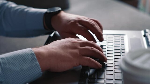 Male hands typing on laptop next to coffee cup during remote work completing online tasks and business communication in calm home environment
