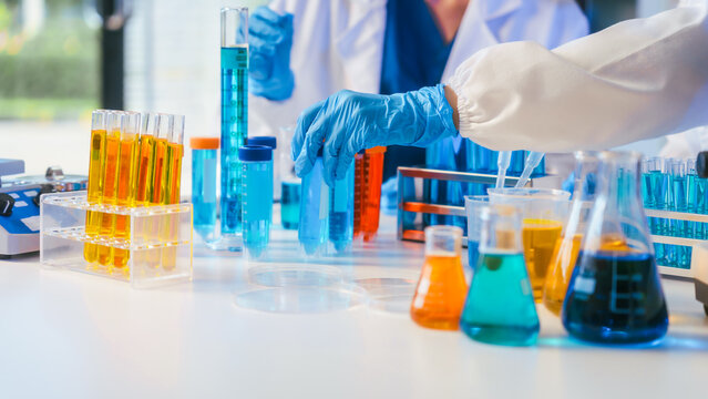 Scientist wearing blue gloves handles colorful test tubes and lab glassware on a clean laboratory bench during a research experiment