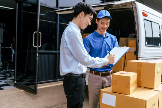 Two men check parcels with a clipboard beside a delivery van and stacked boxes outside a warehouse
